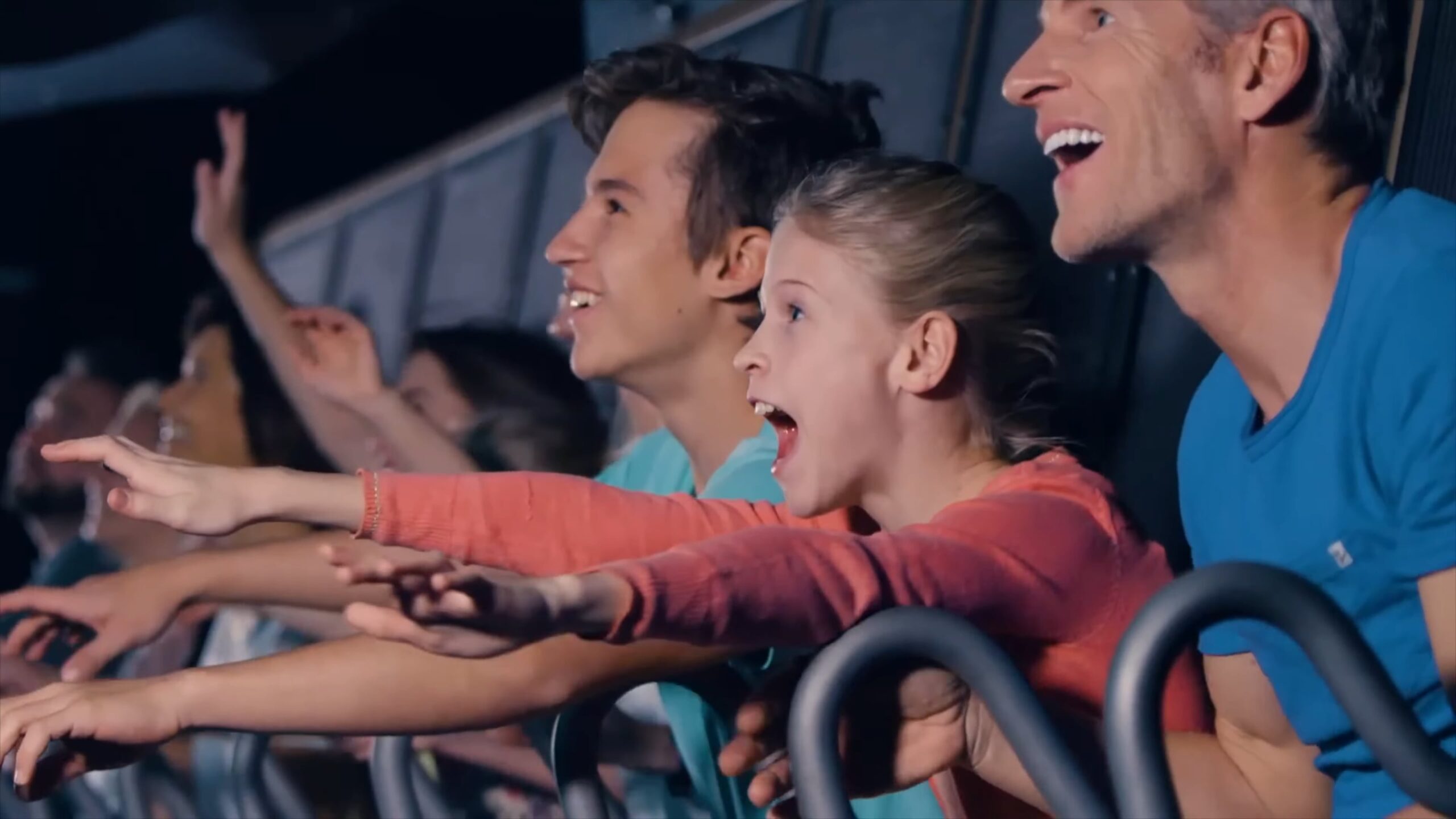 A group of people, including a young girl and a man, excitedly reaching out while experiencing a theme park attraction